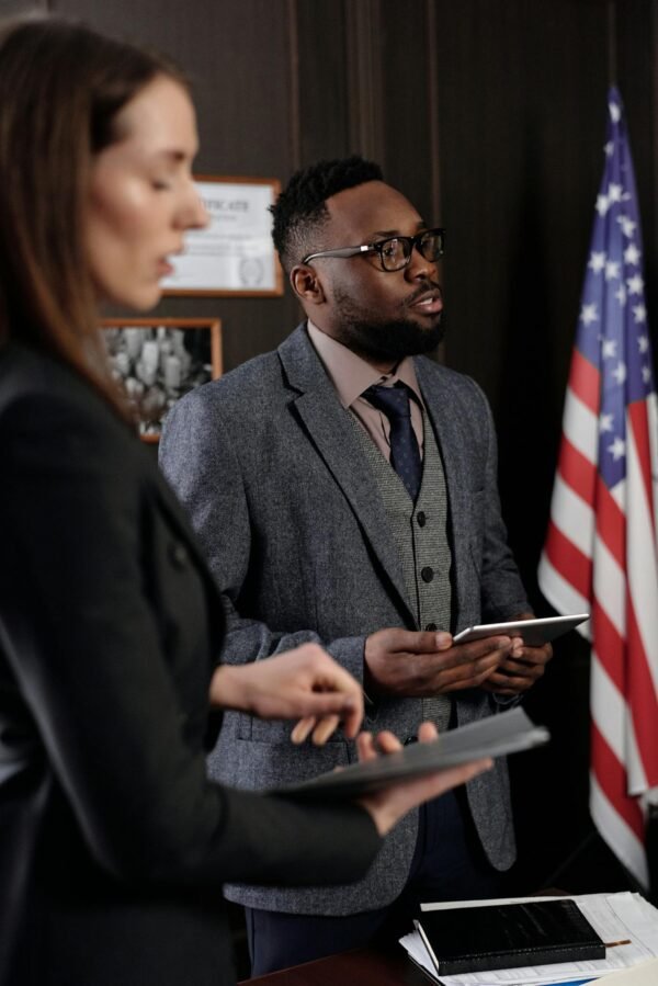 Business professionals discussing in an office with American flag backdrop, conveying a diplomatic setting.