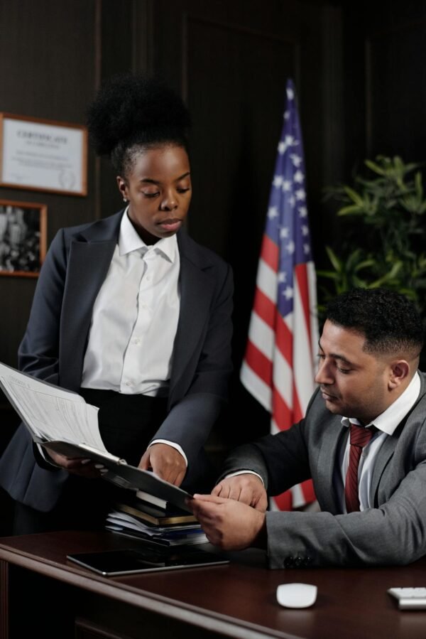 Two professionals reviewing documents in an office with an American flag in the background.